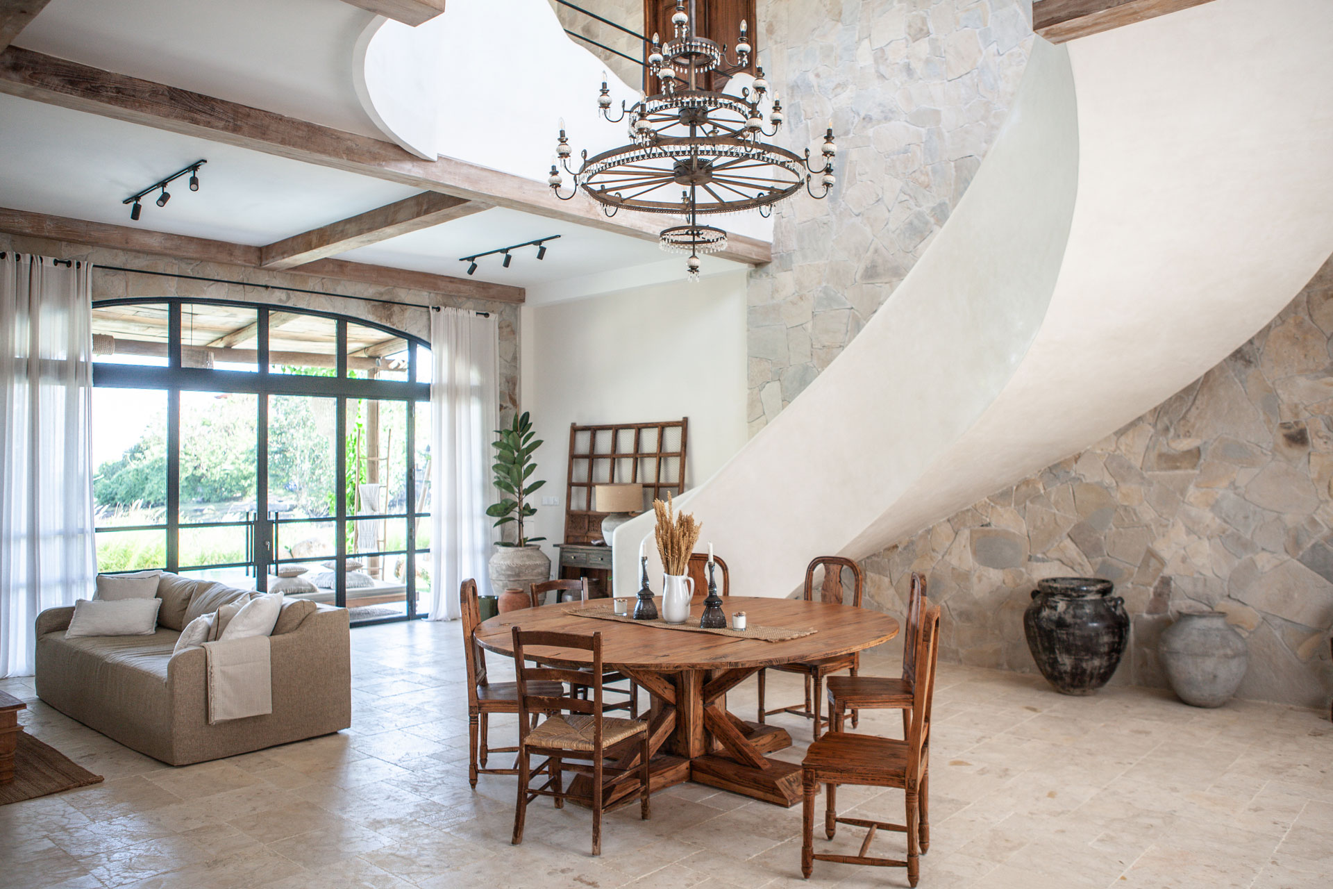 Mediterranean villa living and dining room with a sculpted staircase, designed by Paz Studio Bali